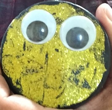 This image shows a glittery, golden hockey puck with googly eyes. It is a placeholder for a picture of a person.